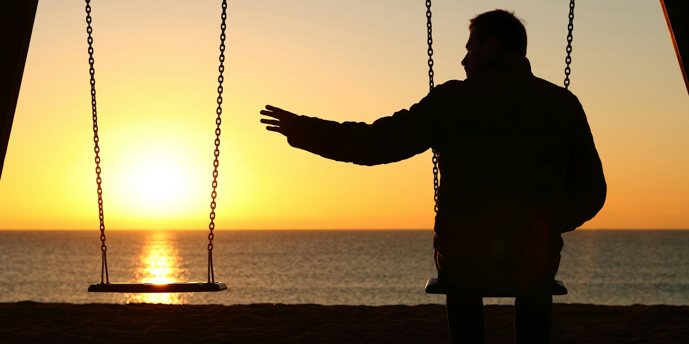 lonely man on swing set reaching arm out to empty seat in front of sunset over water