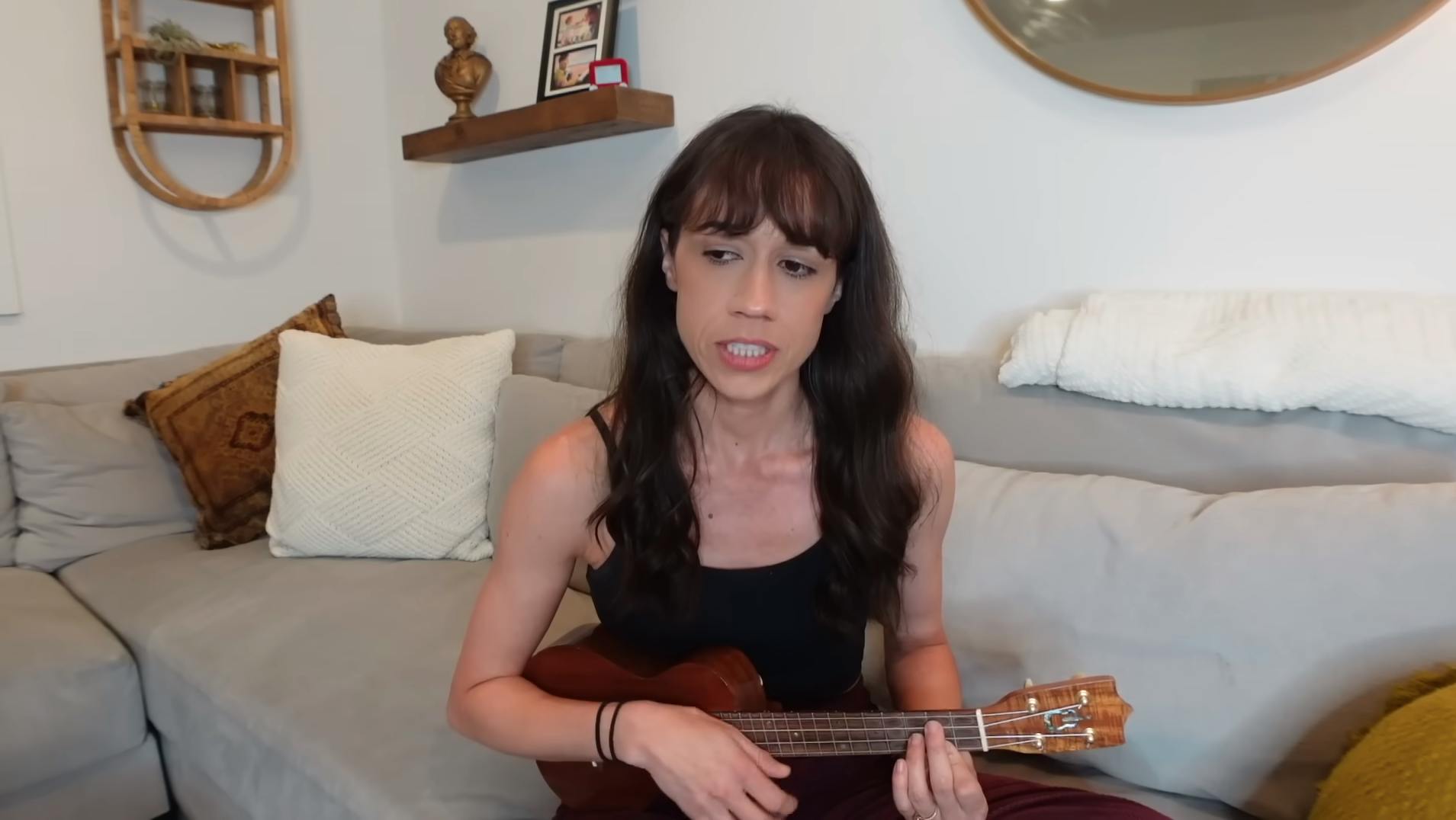 colleen ballinger sings an apology while playing the ukelele on a couch