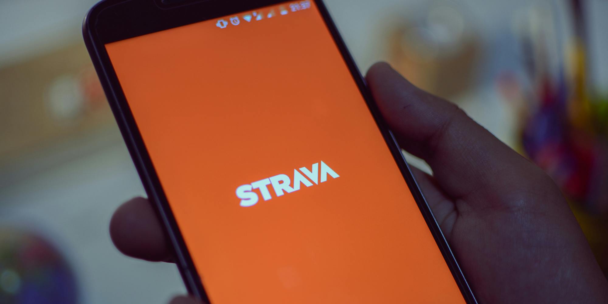 Strava fitness tracker app on phone screen in hand in front of blurred background