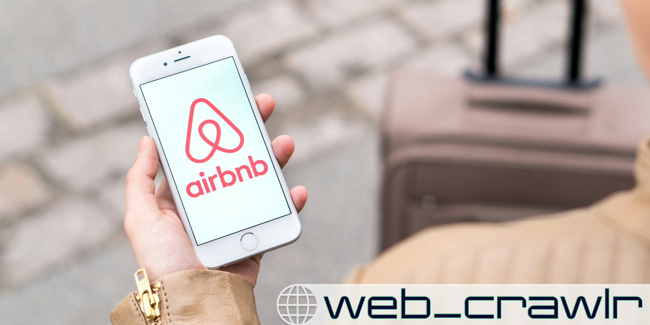 A person holding a phone with the Airbnb logo on it. The Daily Dot newsletter web_crawlr logo is in the bottom right corner.