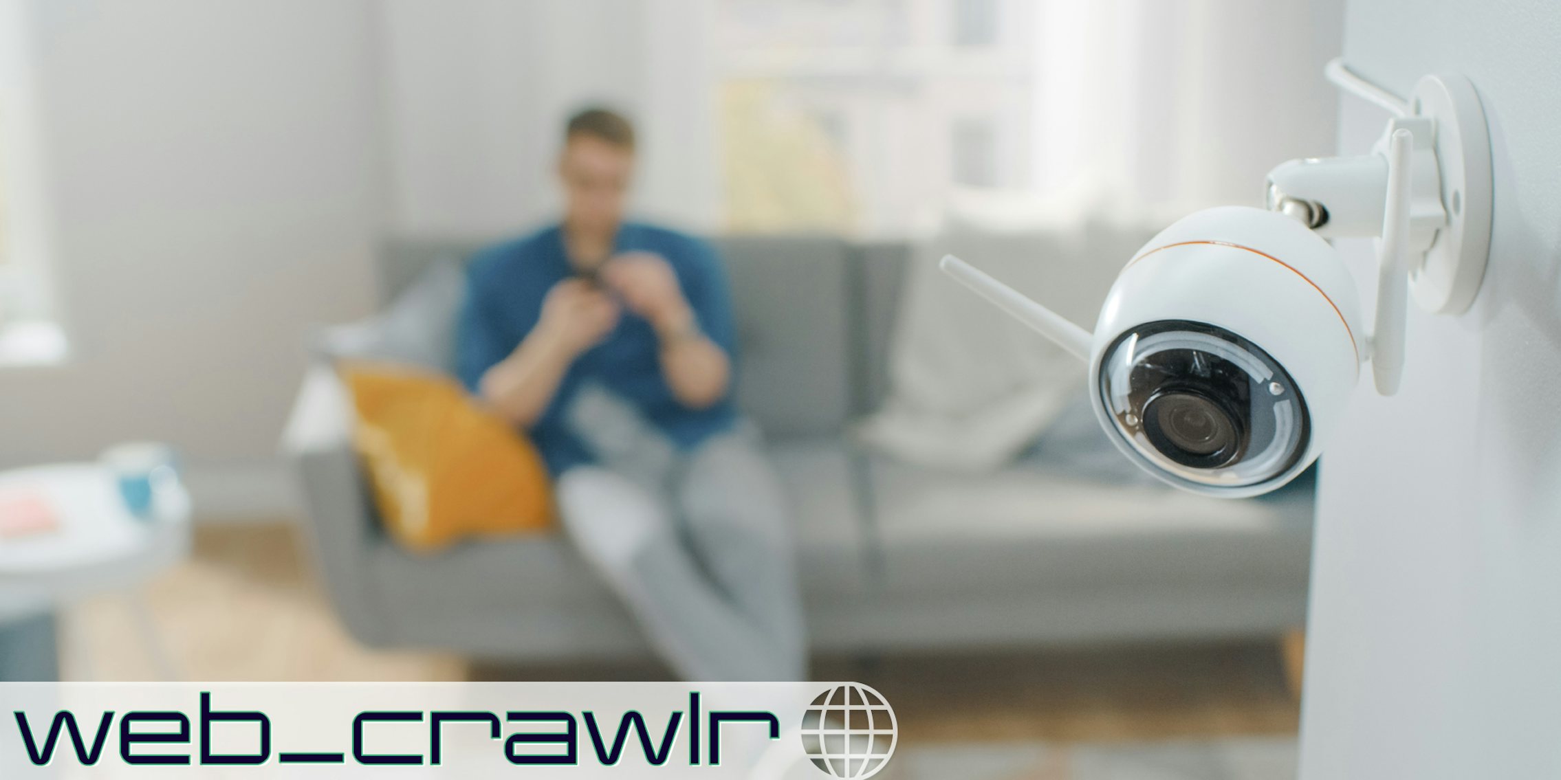 A camera in a living room. A person is sitting on the couch in the background. The Daily Dot newsletter web_crawlr logo is in the bottom left corner.