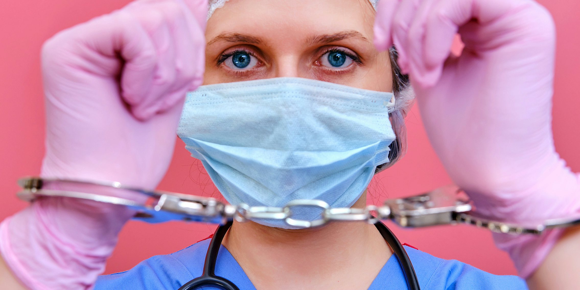 A nurse on a pink background shows hands in handcuffs, closeup.
