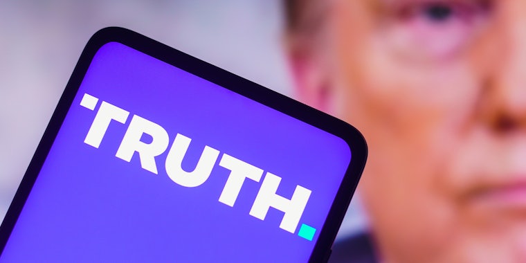 the Truth Social logo seen displayed on a smartphone with a photo of former US President Donald Trump displayed in the background