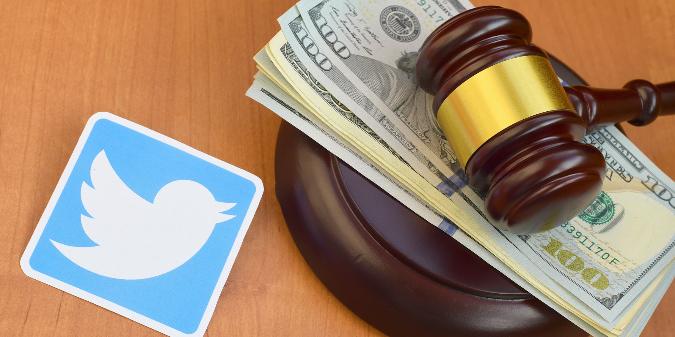 Twitter paper logo lies with judge gavel and hundred dollar bills.