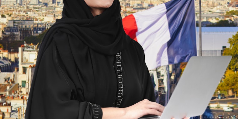 student in abaya holding laptop outside in France