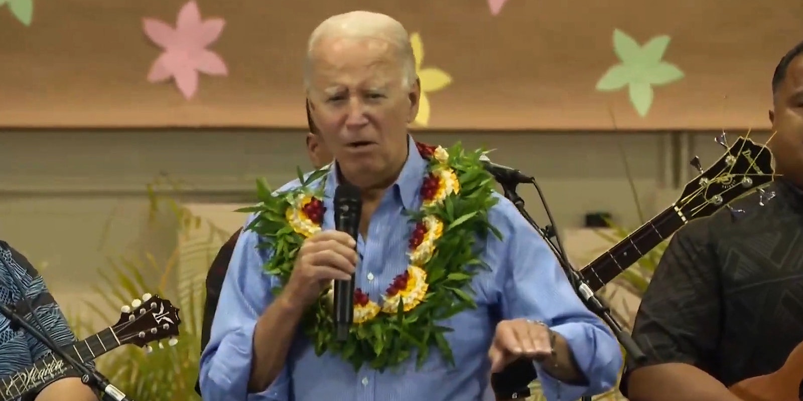 Joe Biden speaking into microphone in front of brown background with flower cutouts