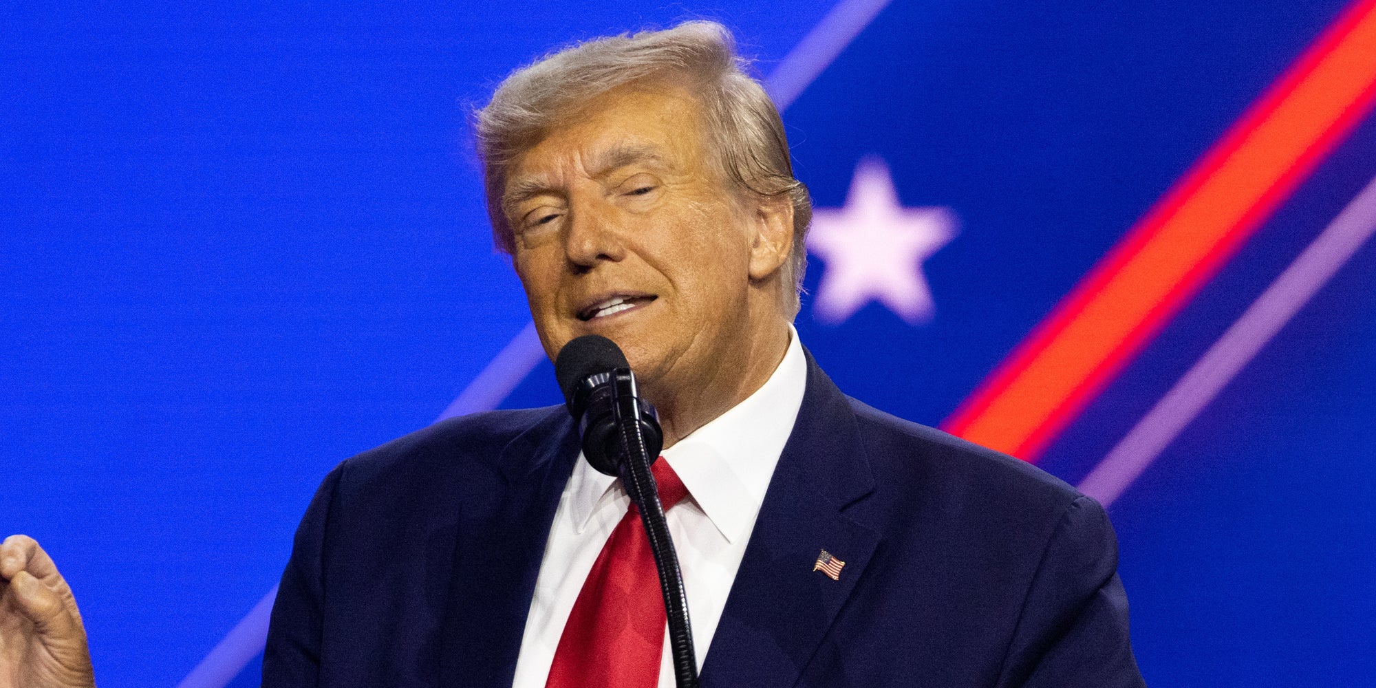 Donald Trump speaking into microphone in front of blue background