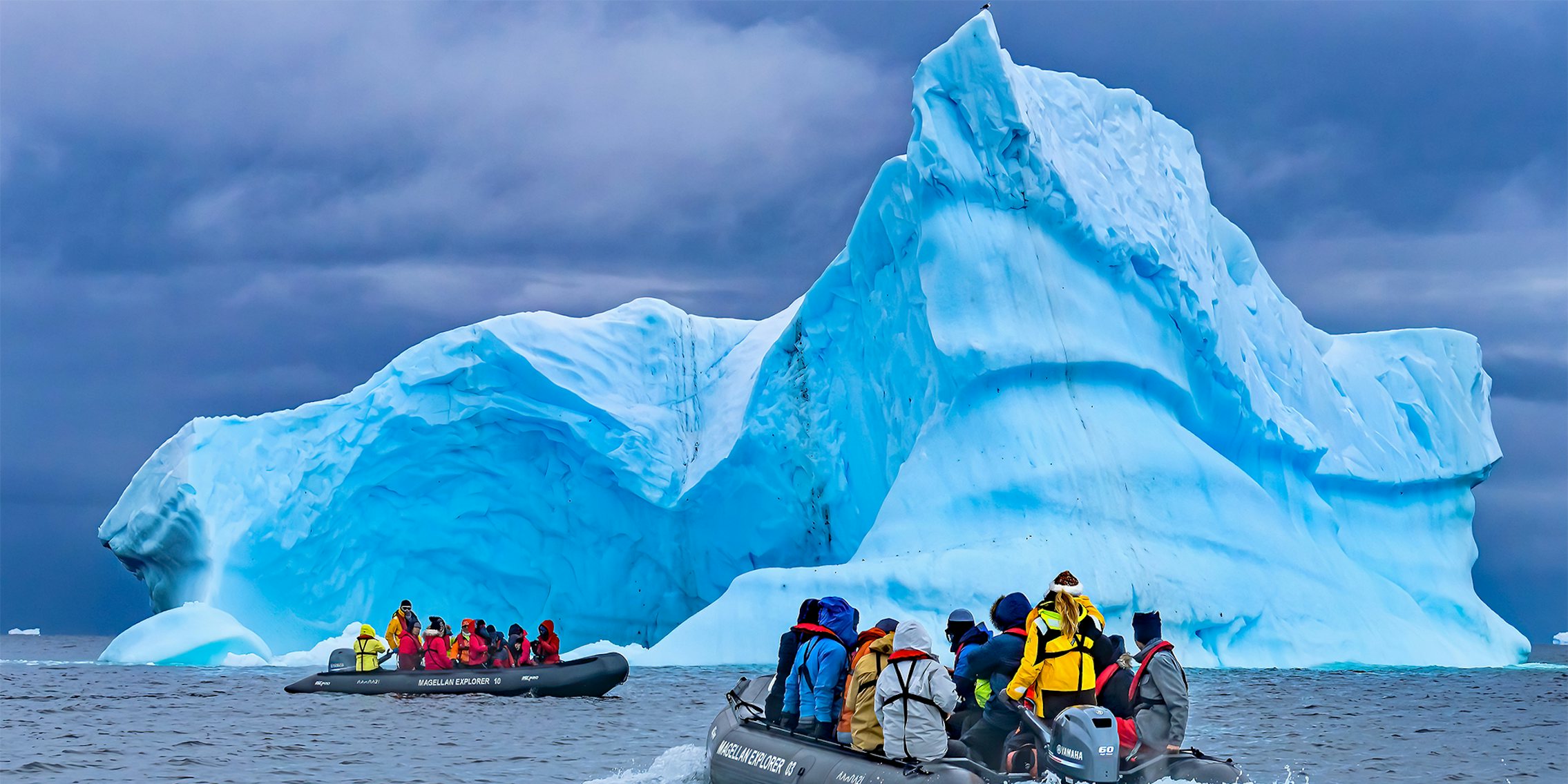 CHARLOTTE BAY, ANTARCTICA - DECEMBER 26, 2019 Tourists Rubber Boats Large Blue Iceberg Charlotte Bay Antarctic Peninsula Antarctica. Glacier ice blue because air squeezed out of snow, which shows that antarctica is real