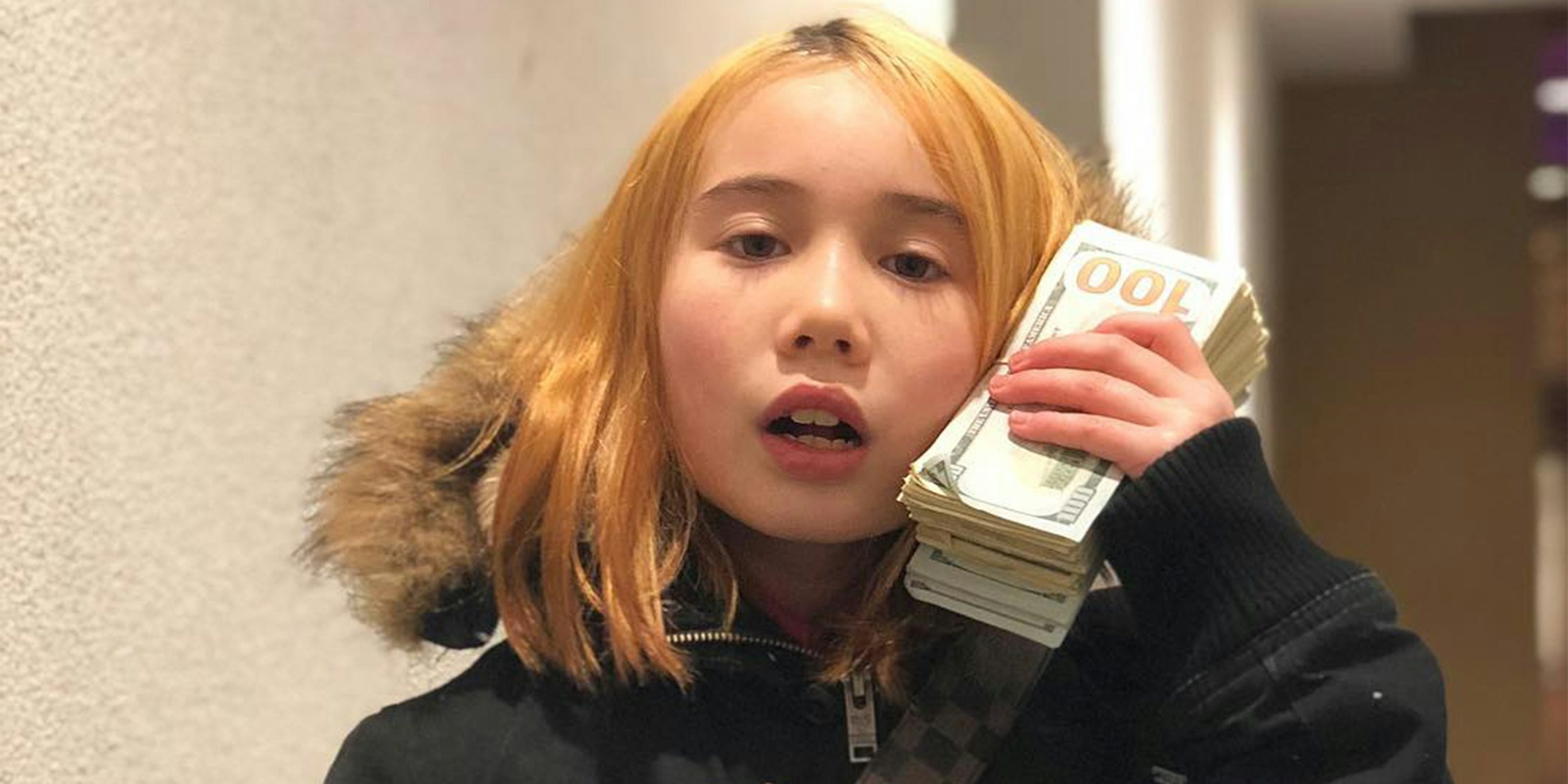 lil Tay with stack of hundred dollar bills up to head like a phone