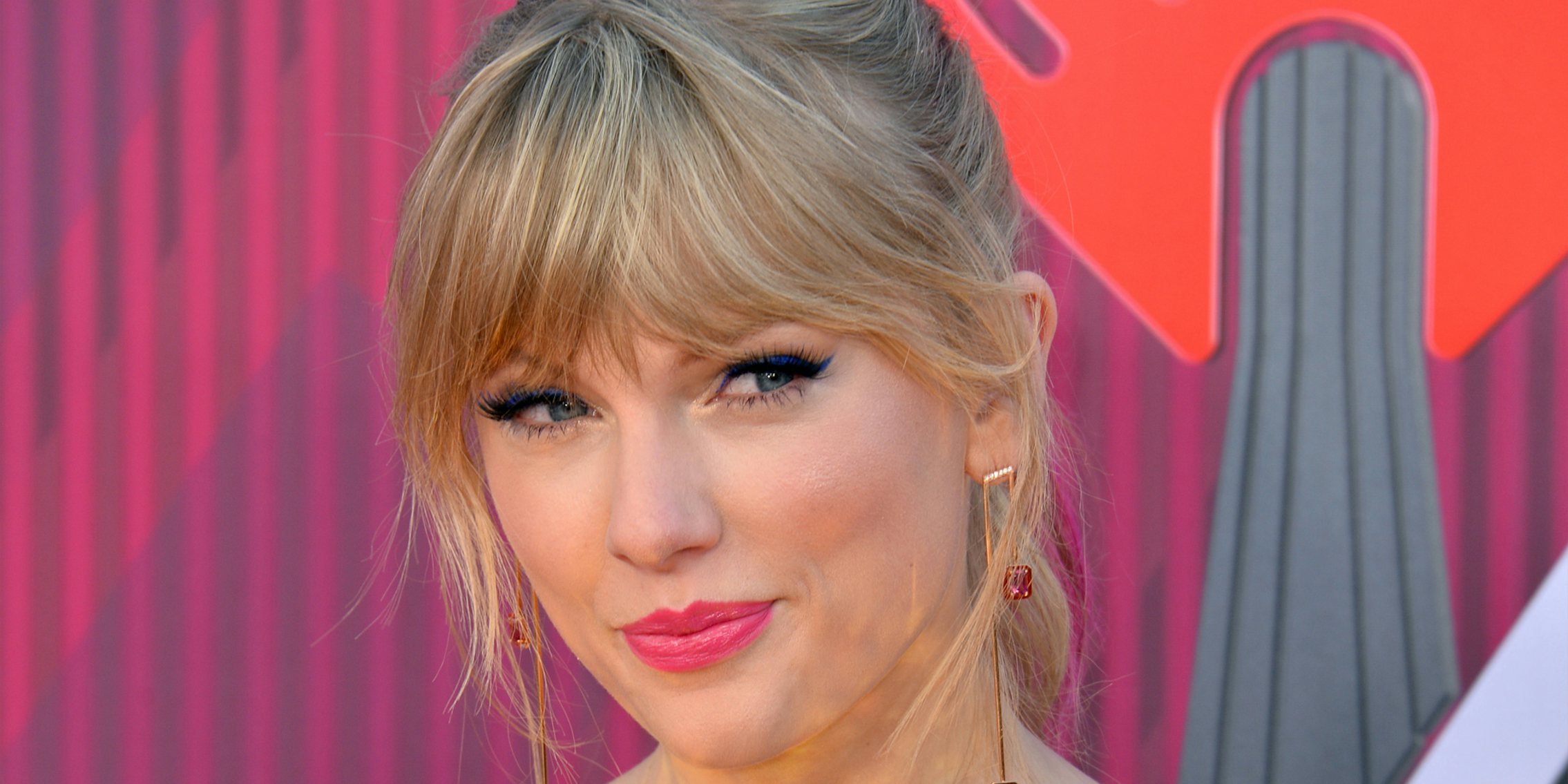 Taylor Swift in front of pink and grey stripe background
