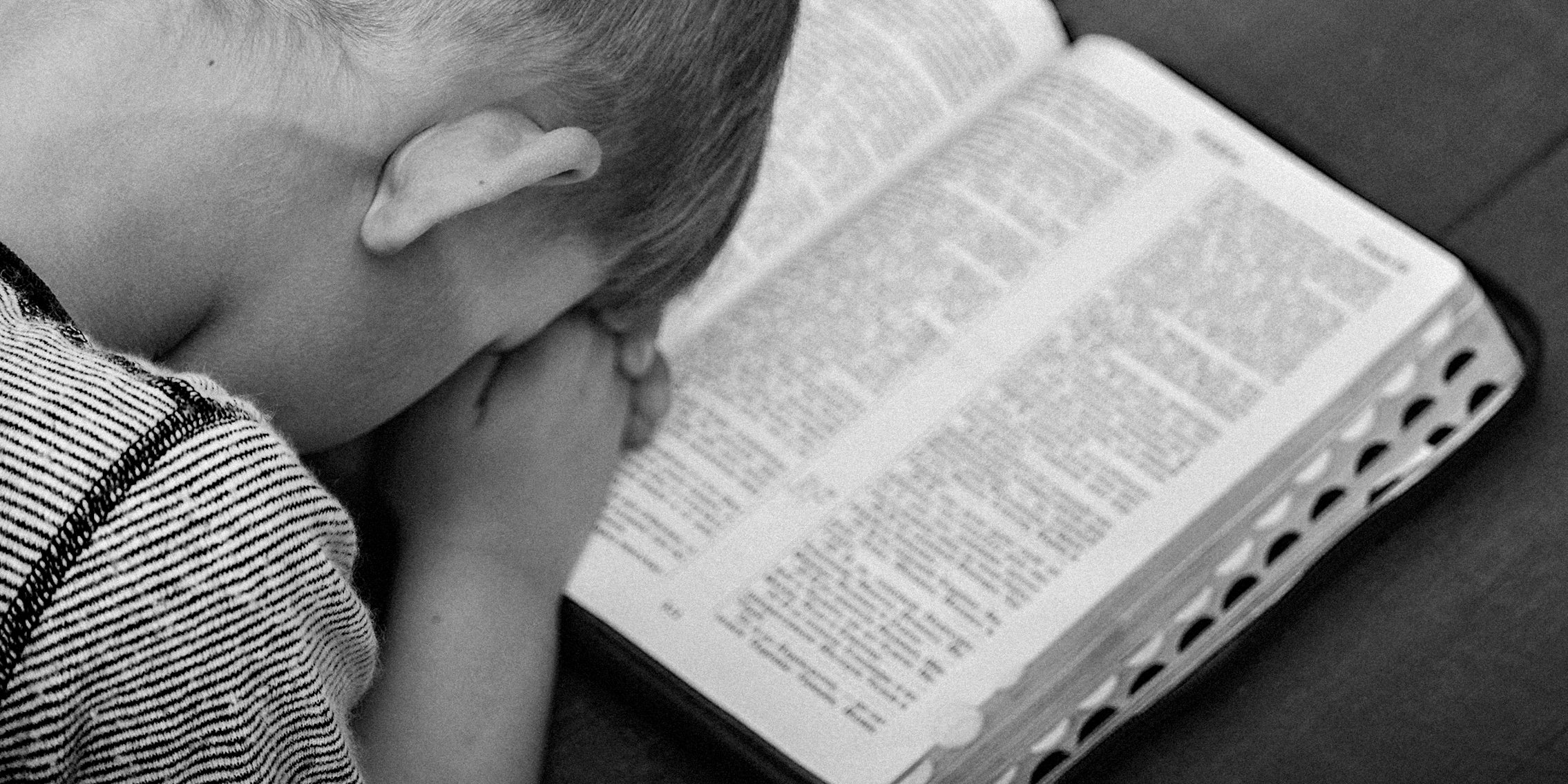 A child prays over open Bible.