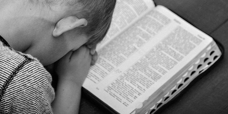 A child prays over open Bible.