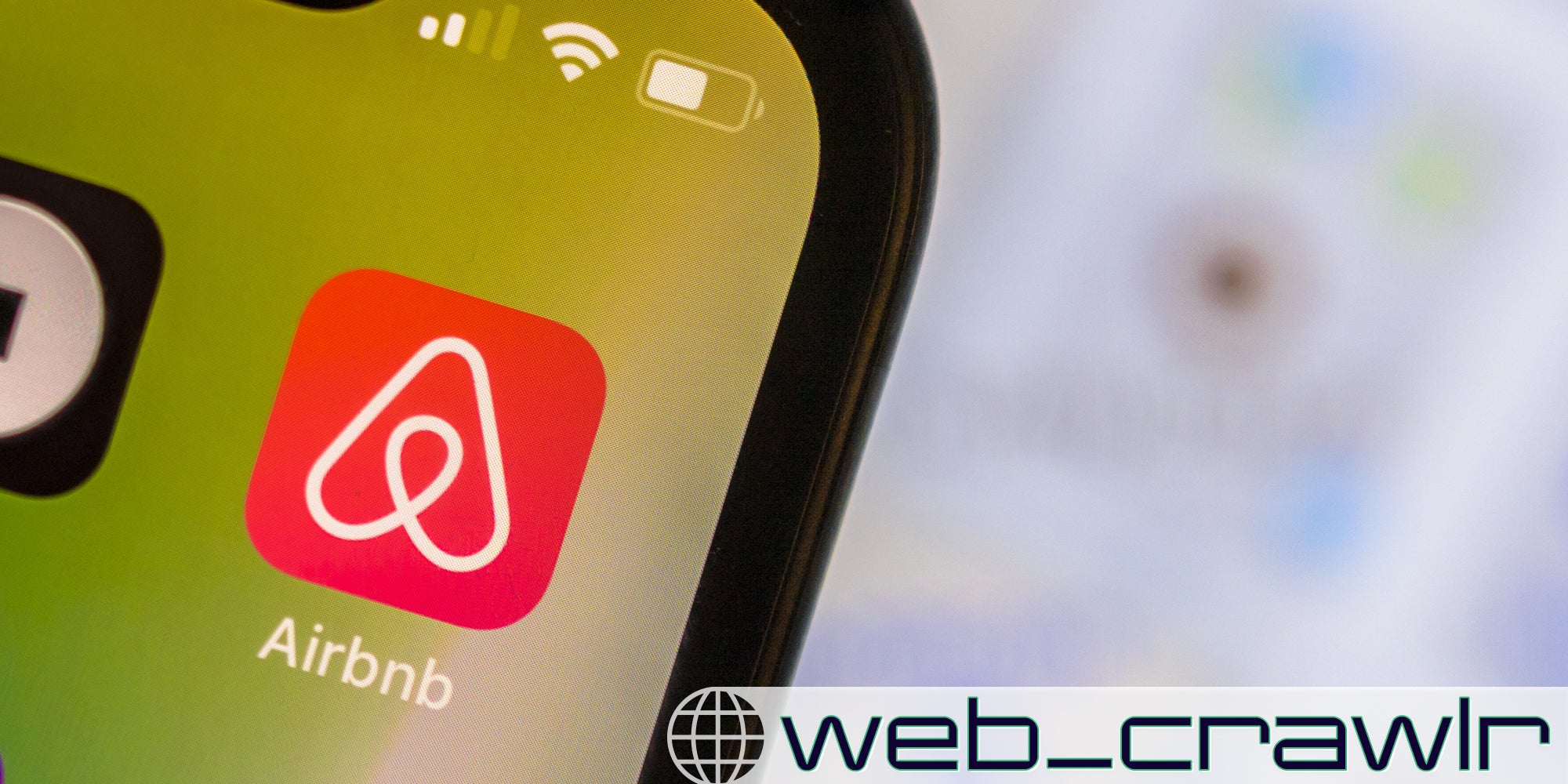 A phone with the Airbnb app on it. The Daily Dot newsletter web_crawlr logo is in the bottom right corner.