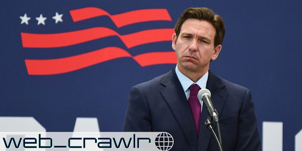 Gov. Ron DeSantis standing at a microphone. The Daily Dot newsletter web_crawlr logo is in the bottom left corner.