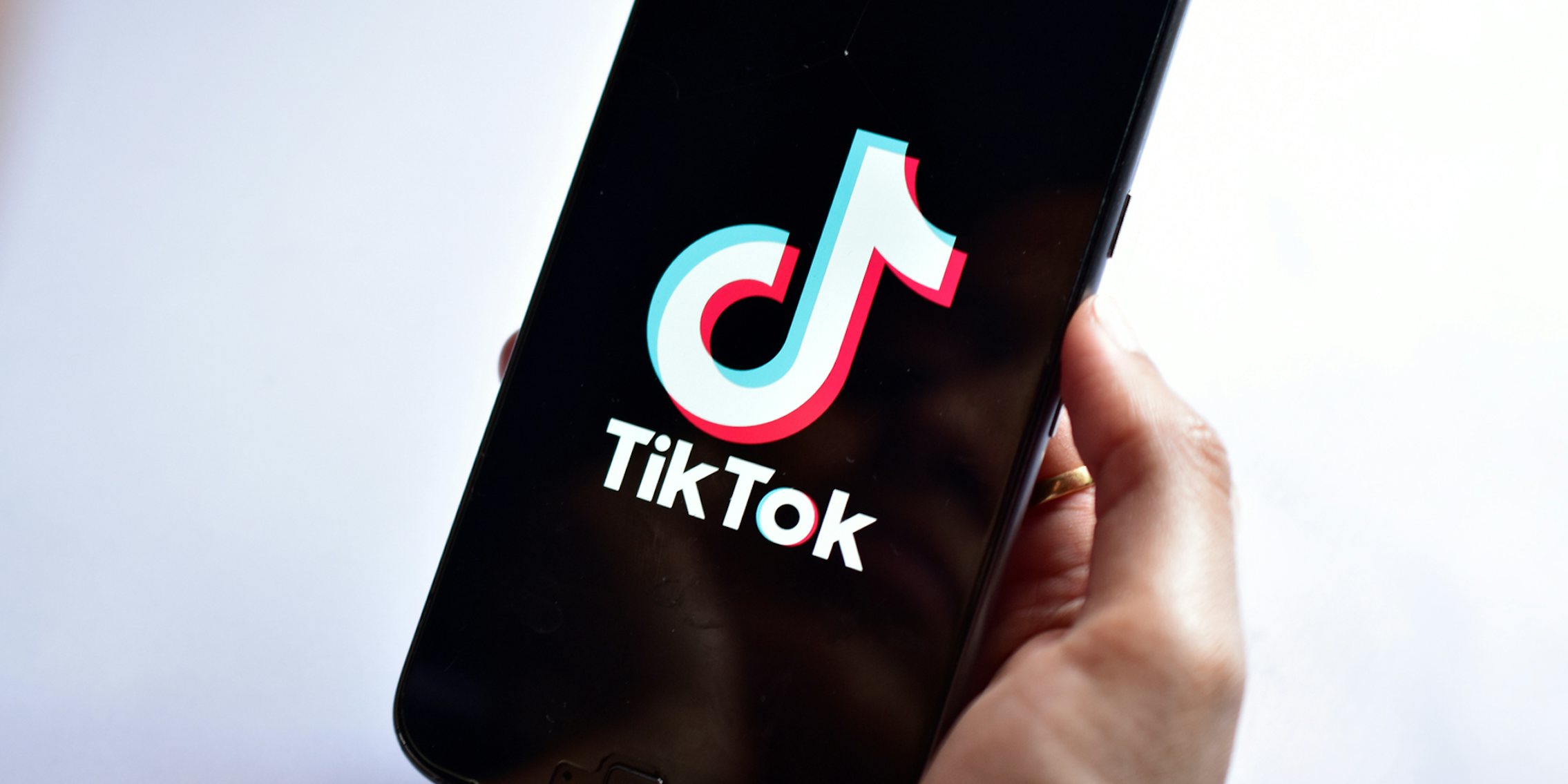 hand holding phone with TikTok on screen in front of light purple to white horizontal gradient background