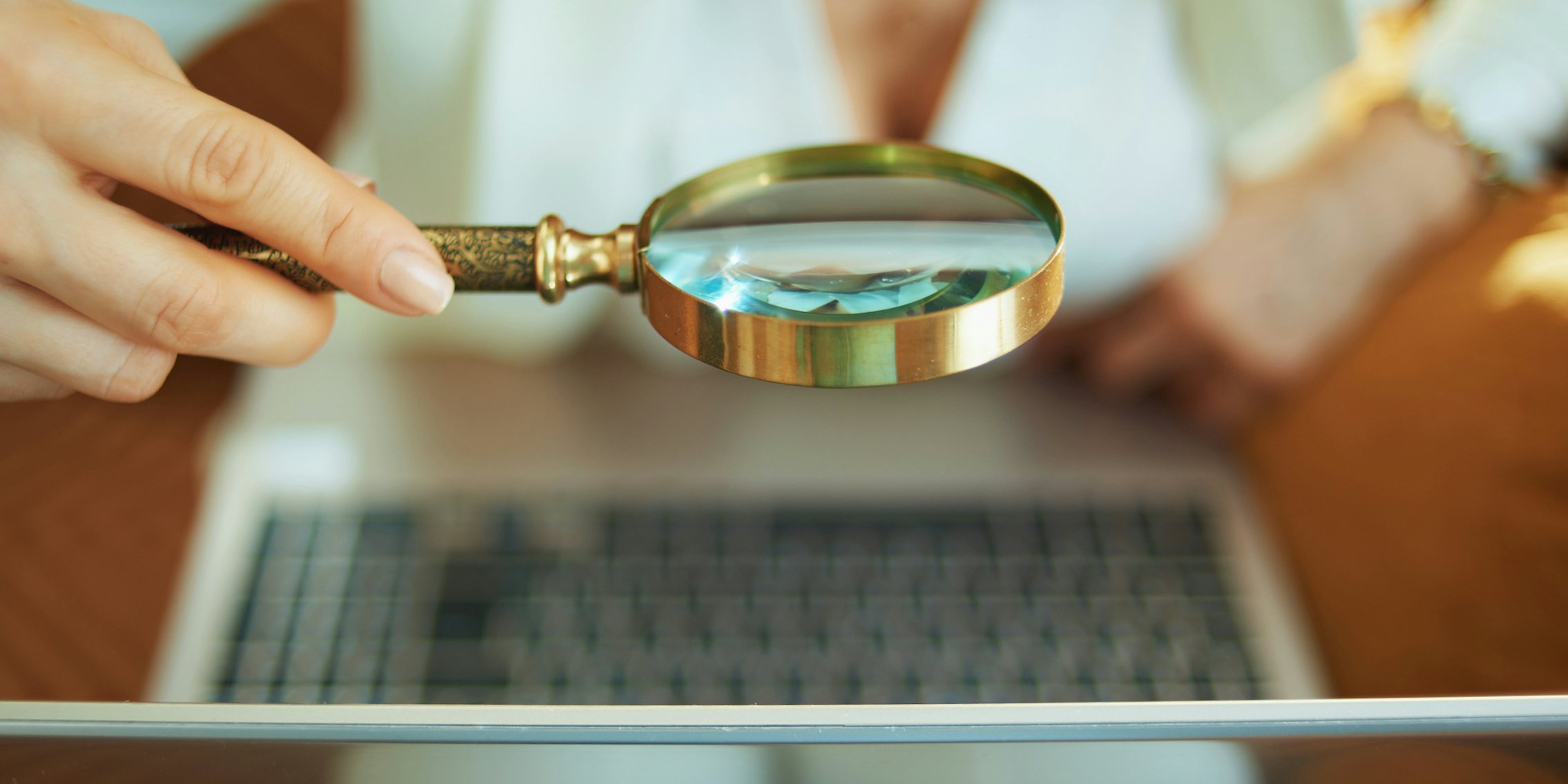 woman holding magnifying glass up to laptop