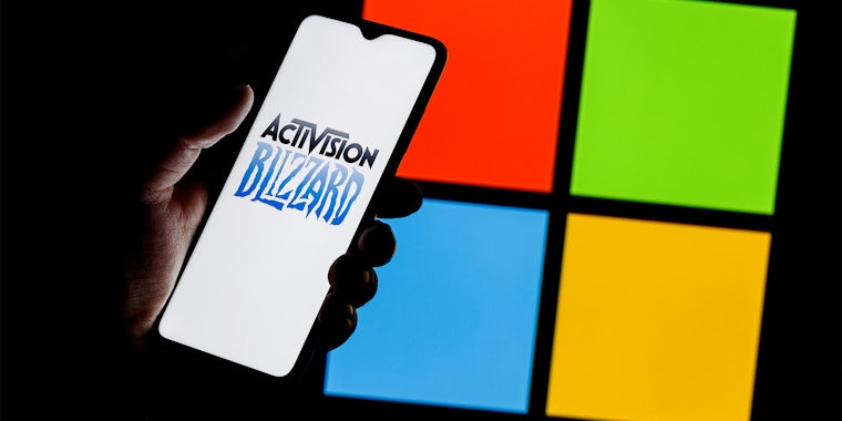 Activision Blizzard logo on smartphone screen in hand against background of Microsoft logo