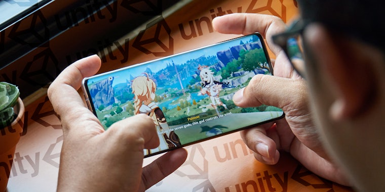 person playing Genshin Impact on phone in front of Unity pattern background
