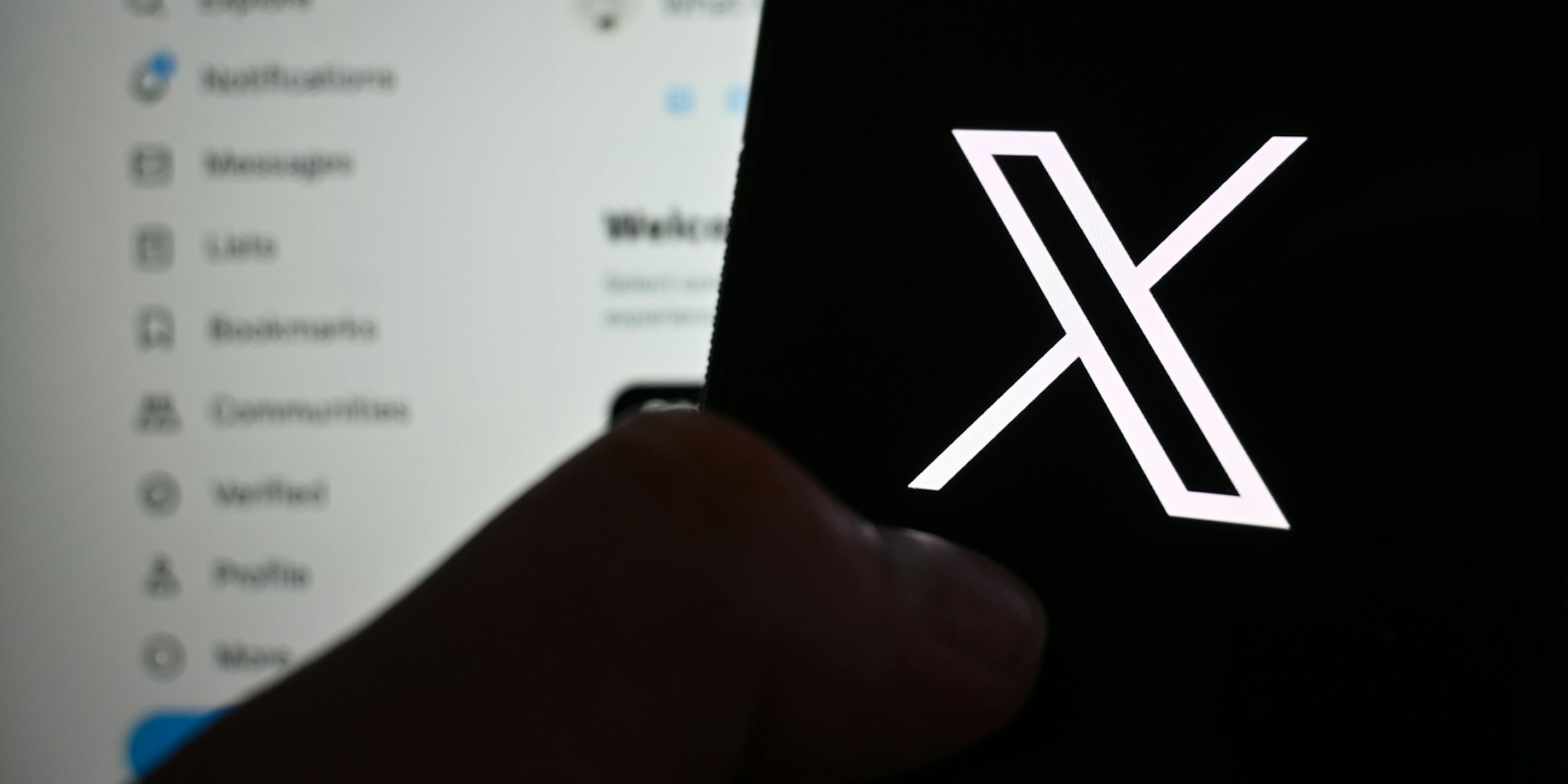 hand holding phone with X logo on screen in front of X open on computer