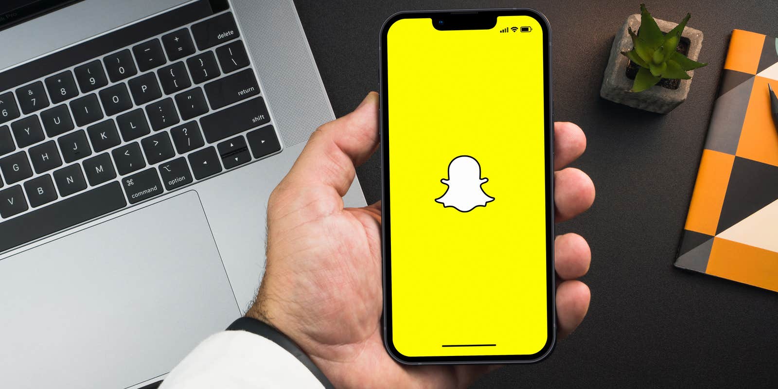 Man holding a smartphone with Snapchat app on the screen on black background table. Office environment.