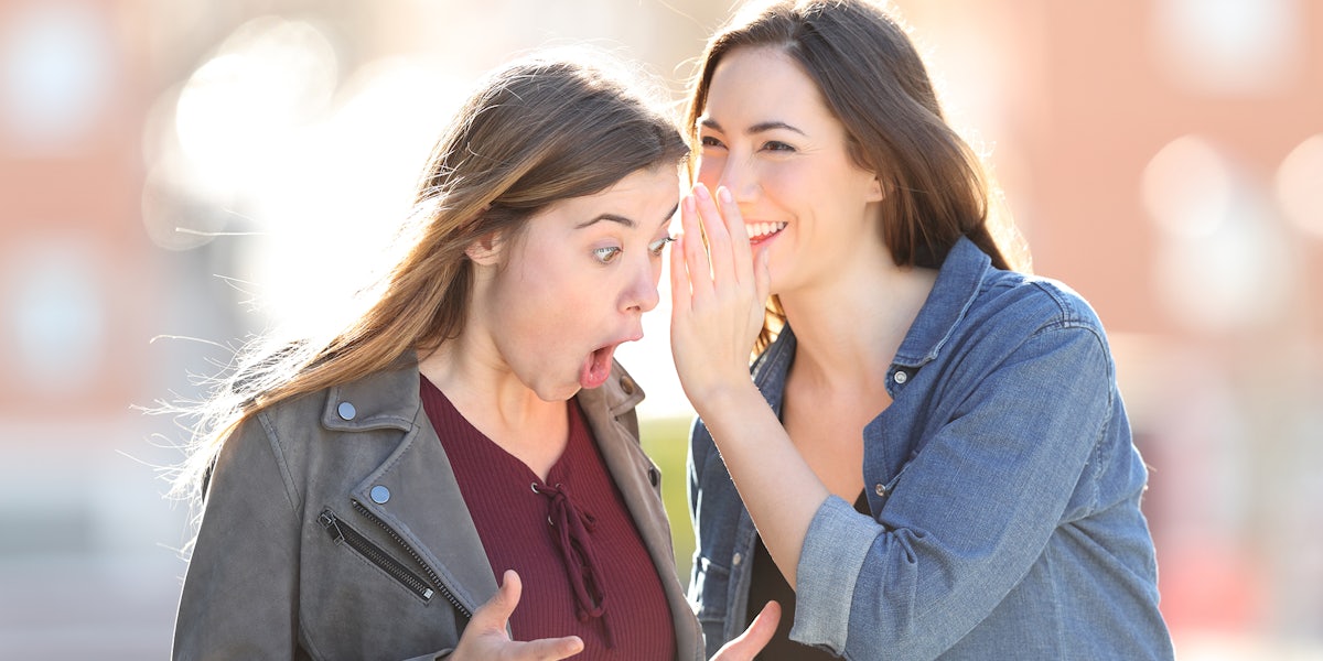 Two gossip girls whispering on ear a secret standing in the street