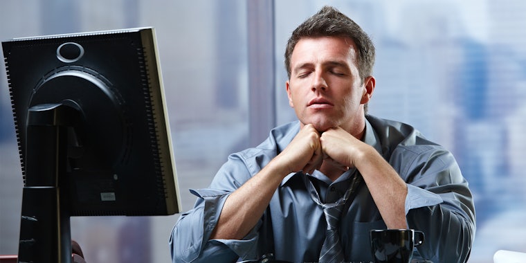 Exhausted businessman focusing on solution of problems sitting at office desk eyes closed.