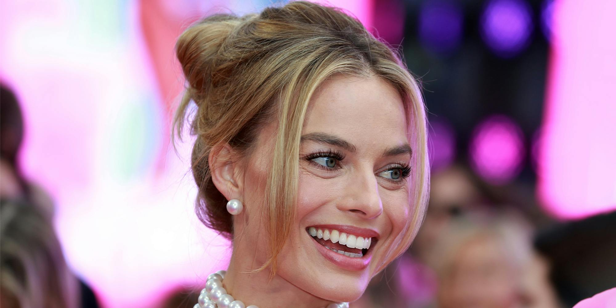 Margot Robbie in front of blurry pink and black background