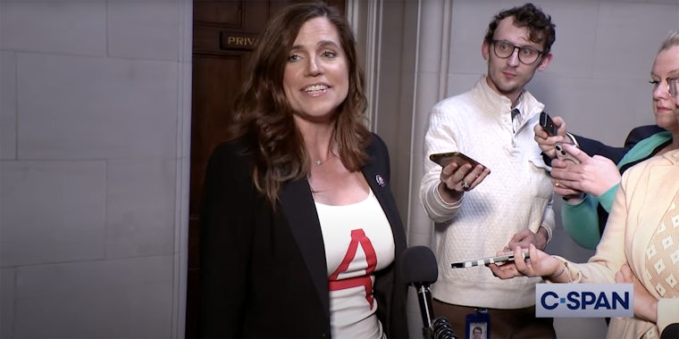 Rep. Nancy Mace wears a white tshirt with a red A on the front while speaking with reporters