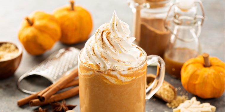 pumpkin spice latte in glass mug in front of pumpkins cinnamon sticks and spices on grey table