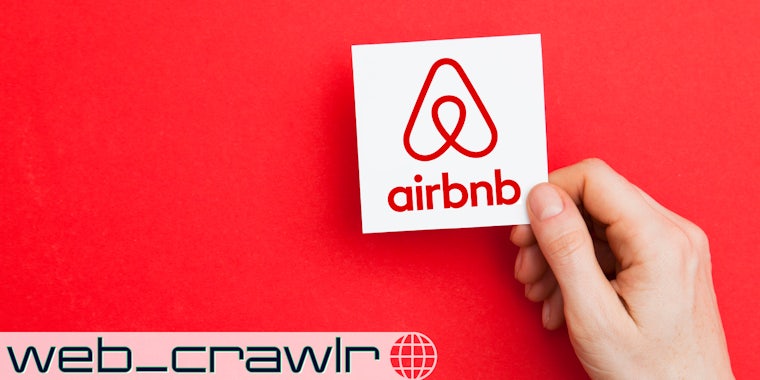 A person holding a card with the Airbnb logo on it. The Daily Dot newsletter web_crawlr logo is in the bottom left corner.