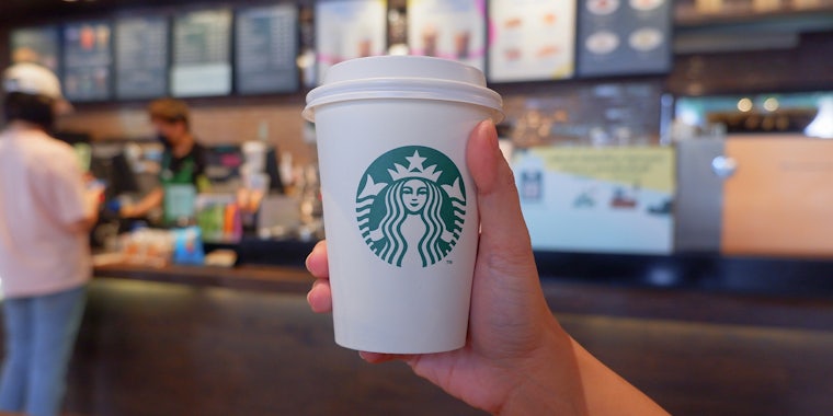 female hand in her 30s holding a cup of hot coffee, Starbucks coffee shop, Chiang Mai, Thailand.