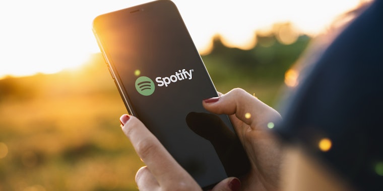 Hand holding phone with spotify app open outdoors
