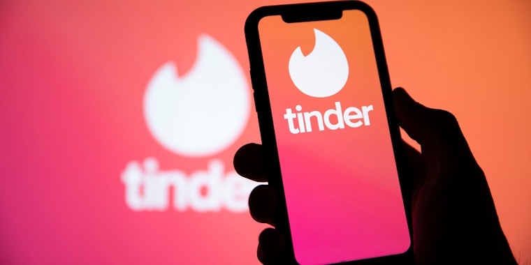 Hand holding phone with tinder on in front of tinder backdrop