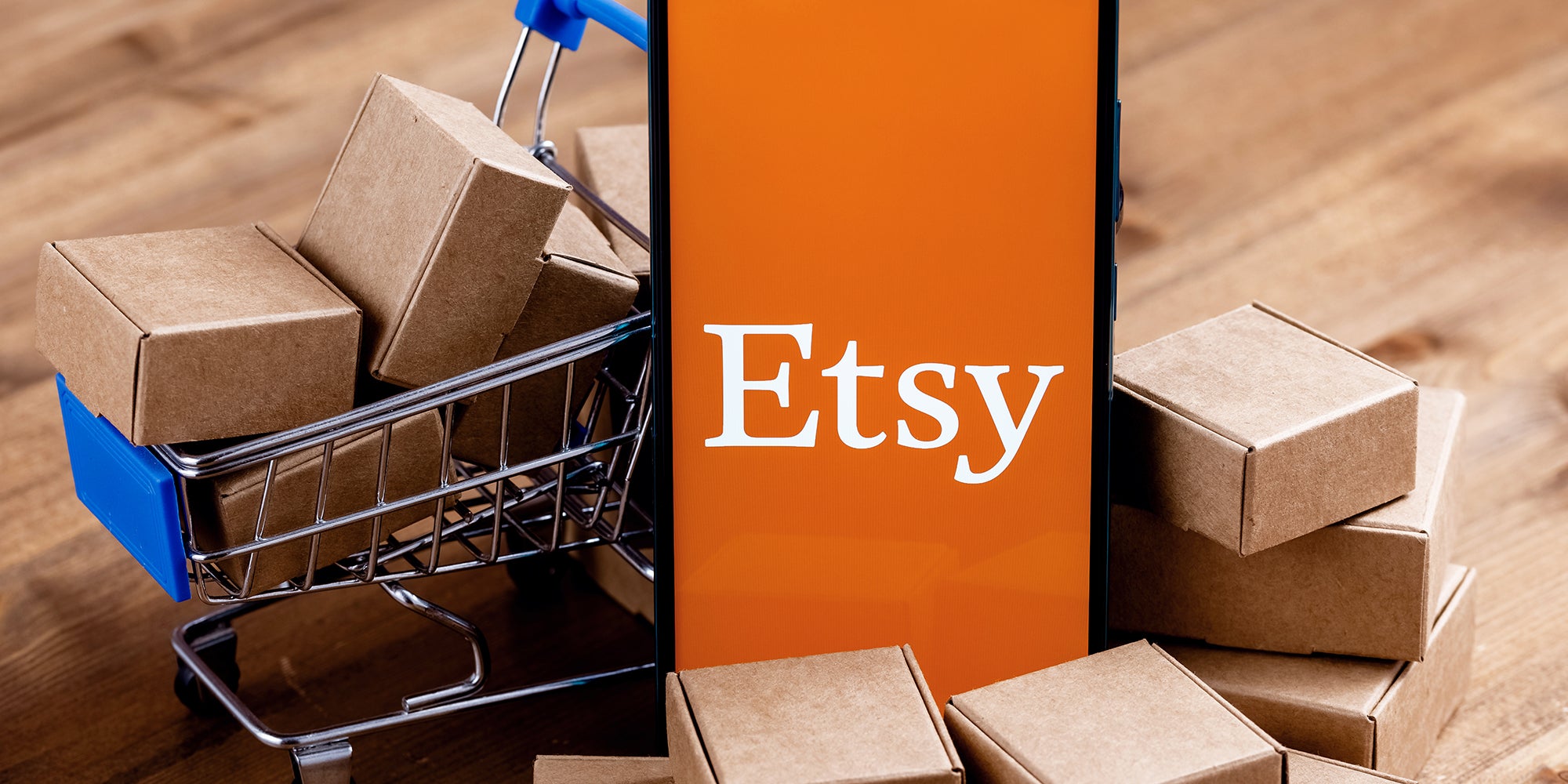 Smartphone with Etsy logo on the screen, shopping cart and parcels.