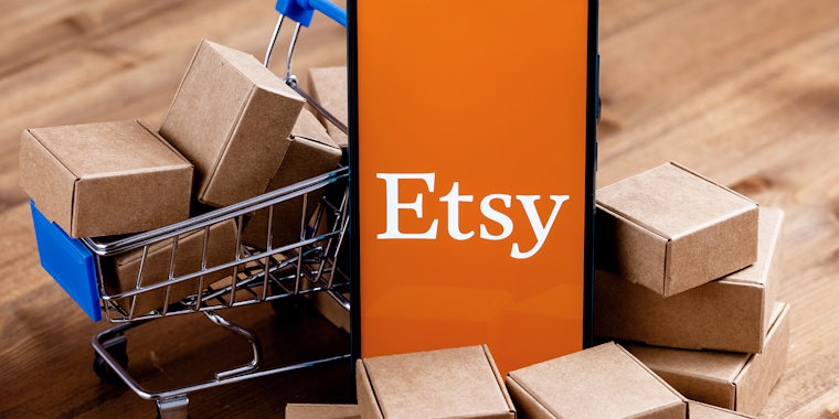 Smartphone with Etsy logo on the screen, shopping cart and parcels.