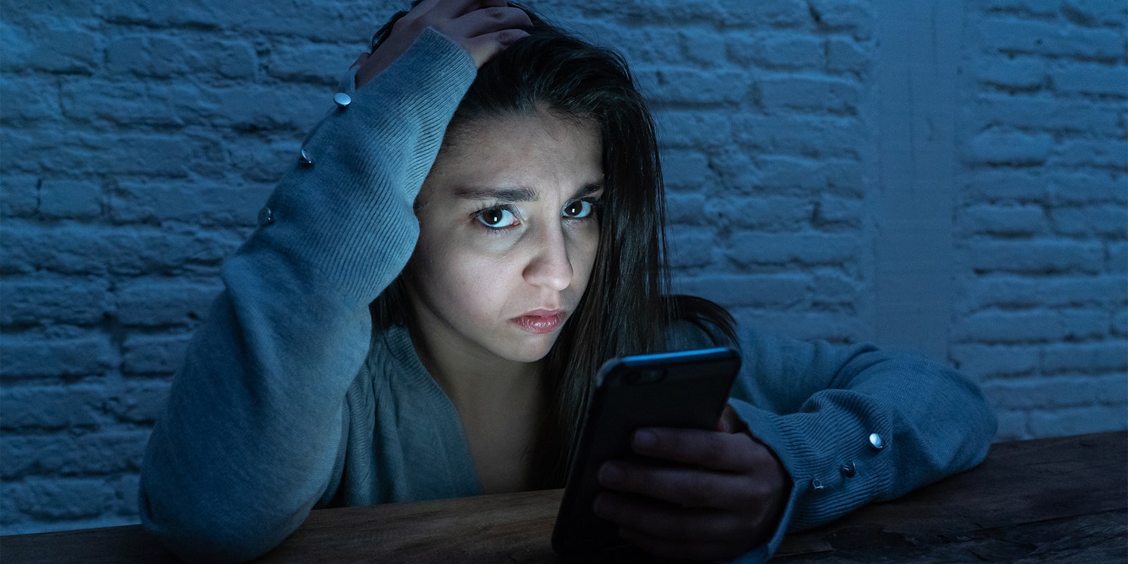 sad scared young woman victim of online harassment and cyberbullying. looking at smart mobile phone