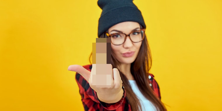 Fashion beauty girl wearing sunglasses, plaid shirt, black beanie hat. Young woman showing middle finger over yellow background.