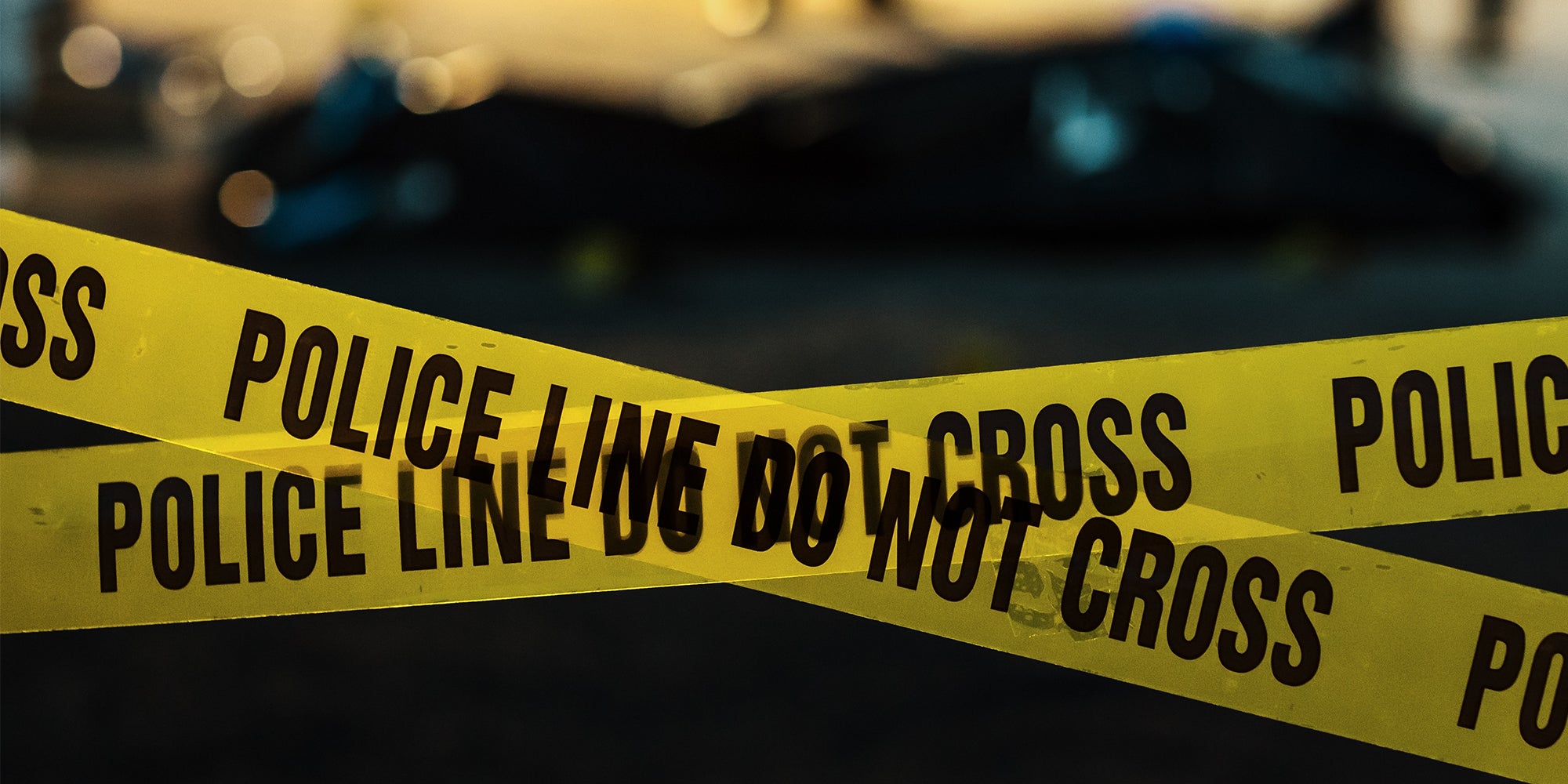 Shot Focused on Yellow Tape Showing Text 'Police Line Do Not Cross'. Tape Used to Restrict a Crime Scene Where Forensics, Detectives and Policemen are Working on Solving a Homicide Case