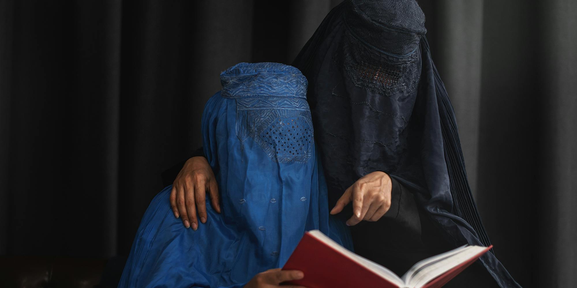 Afghan Muslim women with burka traditional costume, reading holy Quran against the dark background