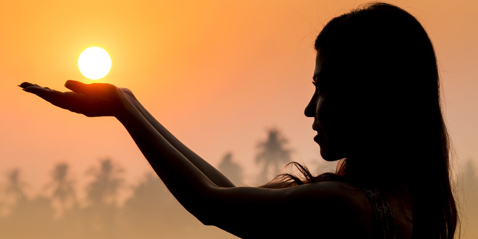 Portrait of young woman as silhouette and hand holding the sun