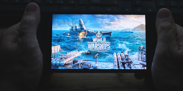 In hand is mobile phone with screensaver logo popular World of Warships game