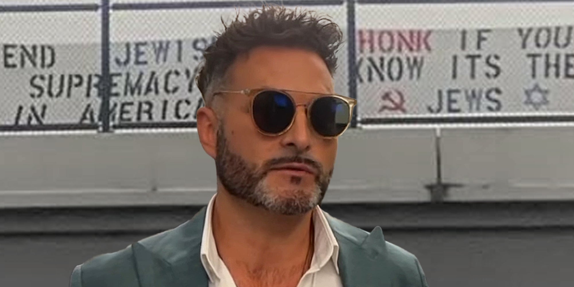 John Minadeo in front of signs hung on highway that read 'end Jewish supremacy in America' and 'Honk if you know its the Jews'