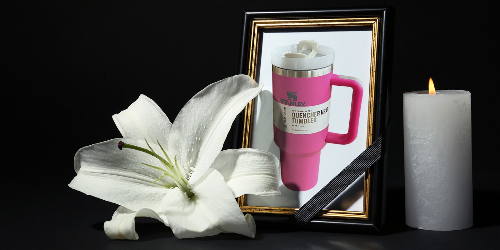 Starbucks Stanley cup in funeral photo frame with ribbon, white lily and candle on dark table against black background