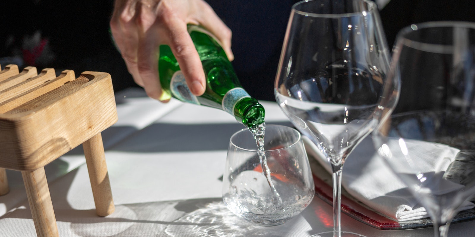 bottle with sparkling water, a hand will pour water into a glass in a restaurant, two empty glasses for wine, on a white tablecloth, lunch with a wine tasting