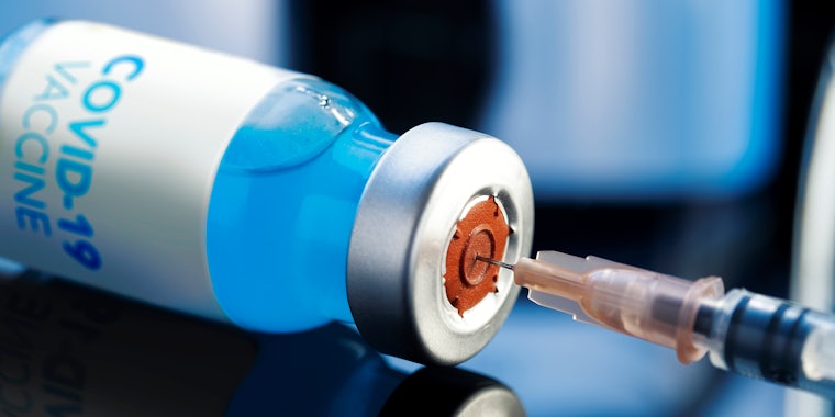 Covid-19 Written vaccine bottle with a blue liquid and taking the vaccine from it with a syringe on a laboratory like background.