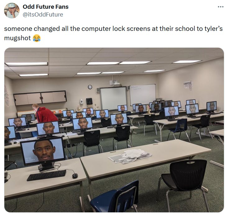 Tweet with a photo of classroom PCs all with a background of Tyler the Creator's mugshot.