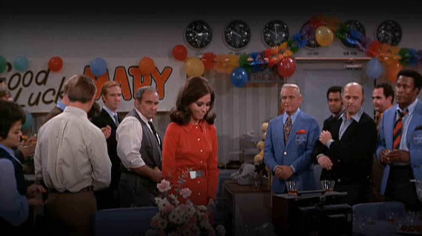 Mary Richards celebrating in the newsroom with her co-workers, including Ted Baxter and Lou Grant, in an episode of 'The Mary Tyler Moore Show.'