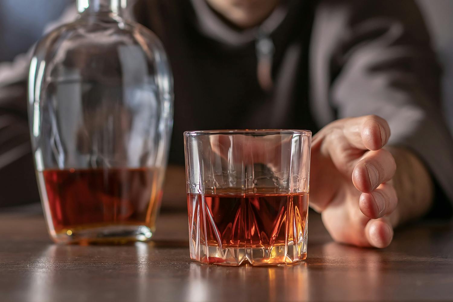 man reaching for a glass of alcohol