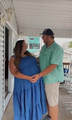 A man and woman standing on a typical American white porch singing to each other as they hold the woman's pregnant belly.