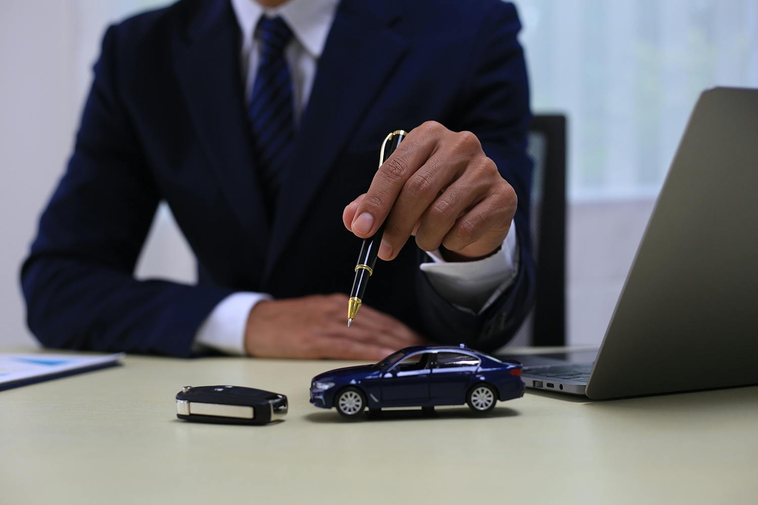 man in suit at desk holding pen over toy car and keys